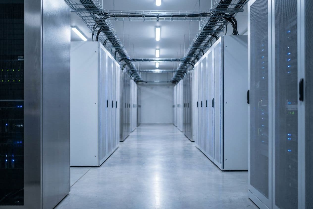 Aisle between rows of server cabinets in a data hall, cable trays running overhead